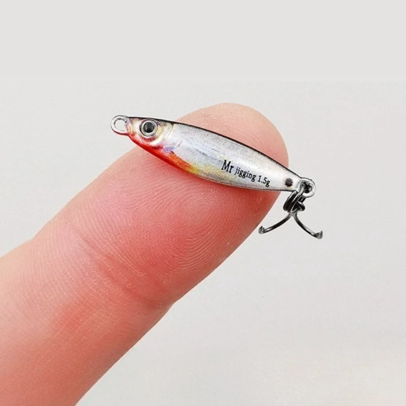 Mini fishing lure with hook, silver and red, balanced on fingertip for size reference.