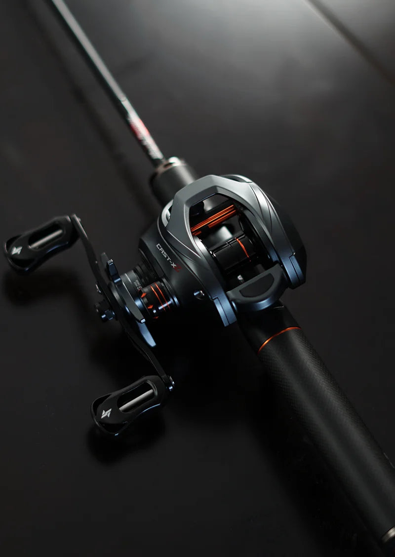 Close-up of a modern black baitcasting fishing reel with orange accents on a dark background