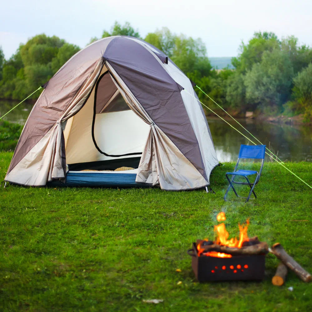 Camping tent with open door by lake, blue chair, and campfire on green grass