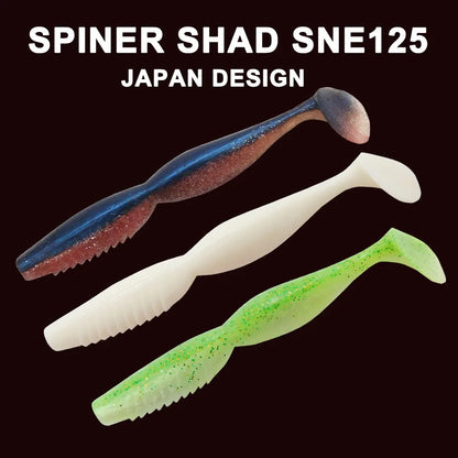 Three SPINER SHAD SNE125 soft plastic fishing lures in blue, white, and green with glitter.