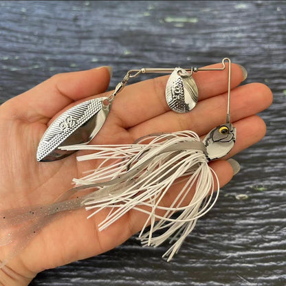 Hand holding silver spinnerbait fishing lure with white and silver skirt, outdoor background.