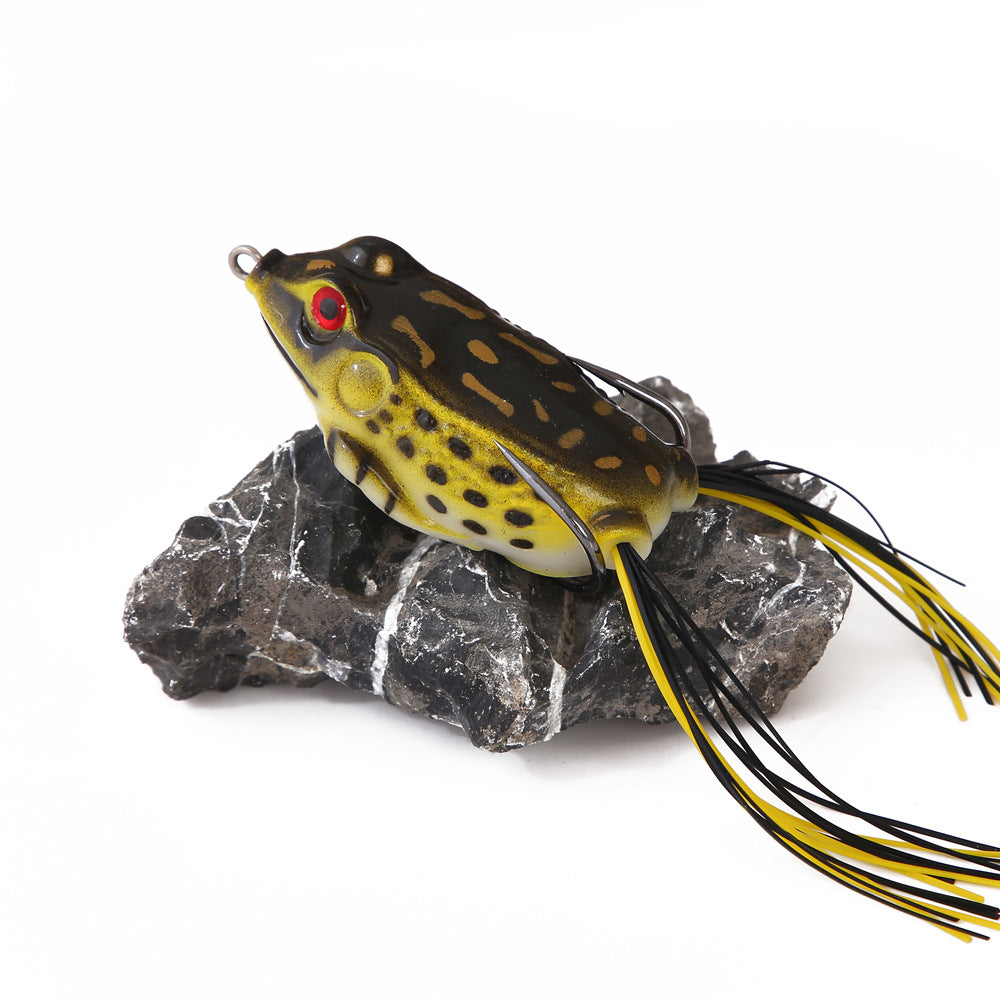 Realistic frog fishing lure with yellow spots and skirted tail on a rock, outdoor gear