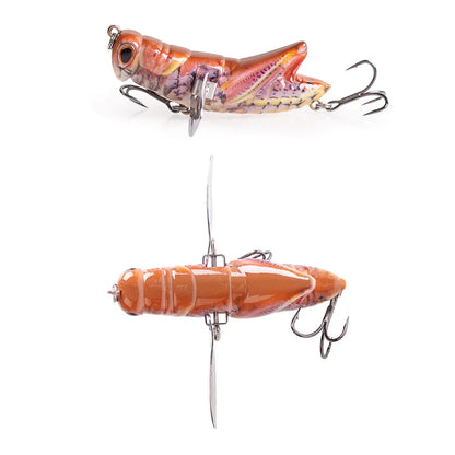 Realistic grasshopper fishing lure with treble hooks and vibrant orange details on white background.