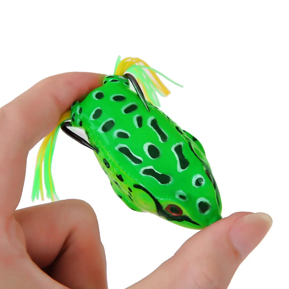 Hand holding green frog-shaped fishing lure with hooks and yellow tail, outdoor gear accessory