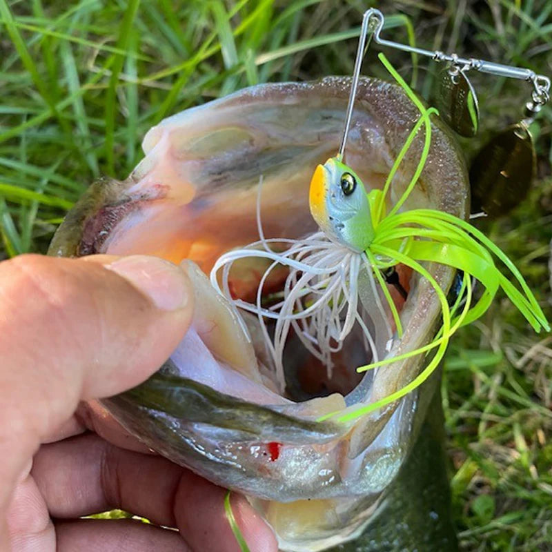 Hand holding largemouth bass with green and yellow fishing lure in its mouth on grass