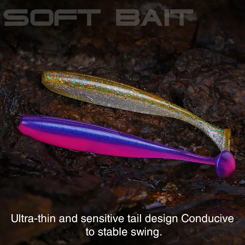 Soft plastic fishing lures in glitter gold and purple-pink, with paddle tails on rocky surface.