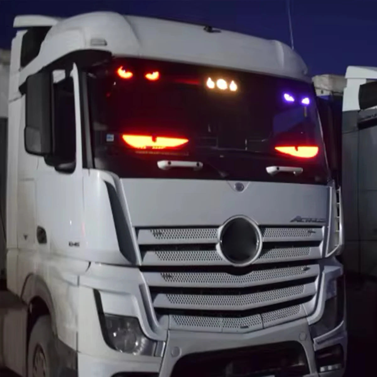 Close-up of a white truck's front grille with visible brand logo at night.