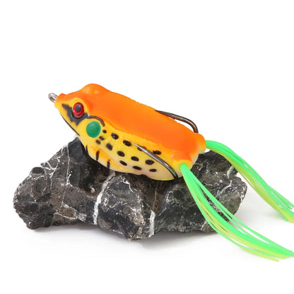 Colorful frog fishing lure with orange, yellow, and green details on a rock, outdoor gear