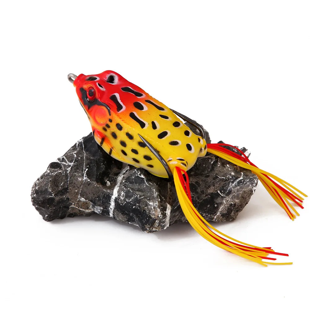 Colorful frog-shaped fishing lure with yellow and red details displayed on a dark rock