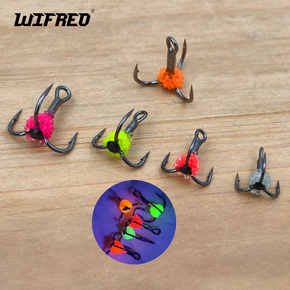 Set of colorful treble fishing hooks with glow-in-the-dark beads on wooden surface