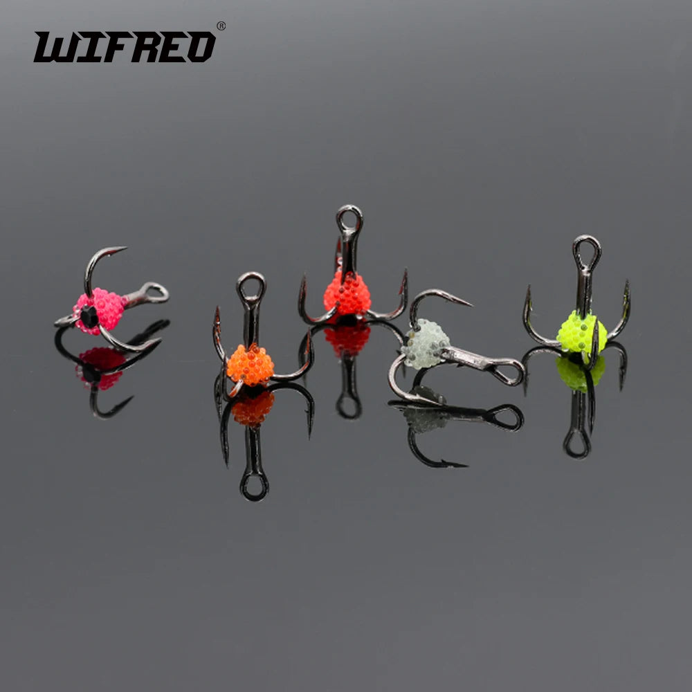 Five colorful treble fishing hooks with bead accents displayed on a reflective black surface.