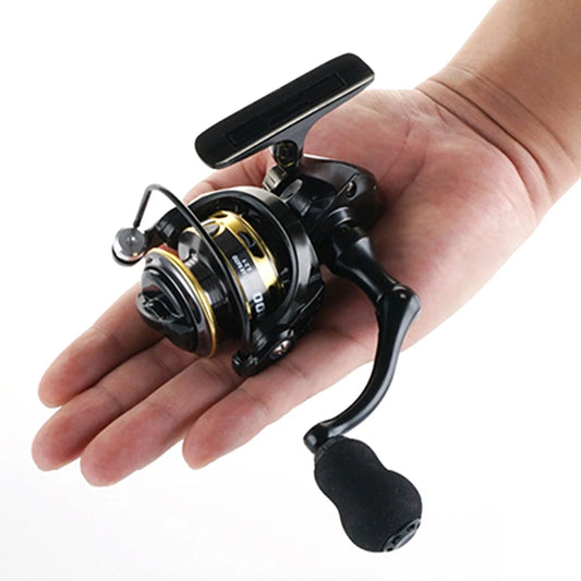 Compact black and gold fishing reel with ergonomic handle held in a person's hand