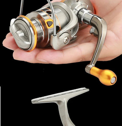 Compact metal fishing reel with orange accents held in a hand on black background