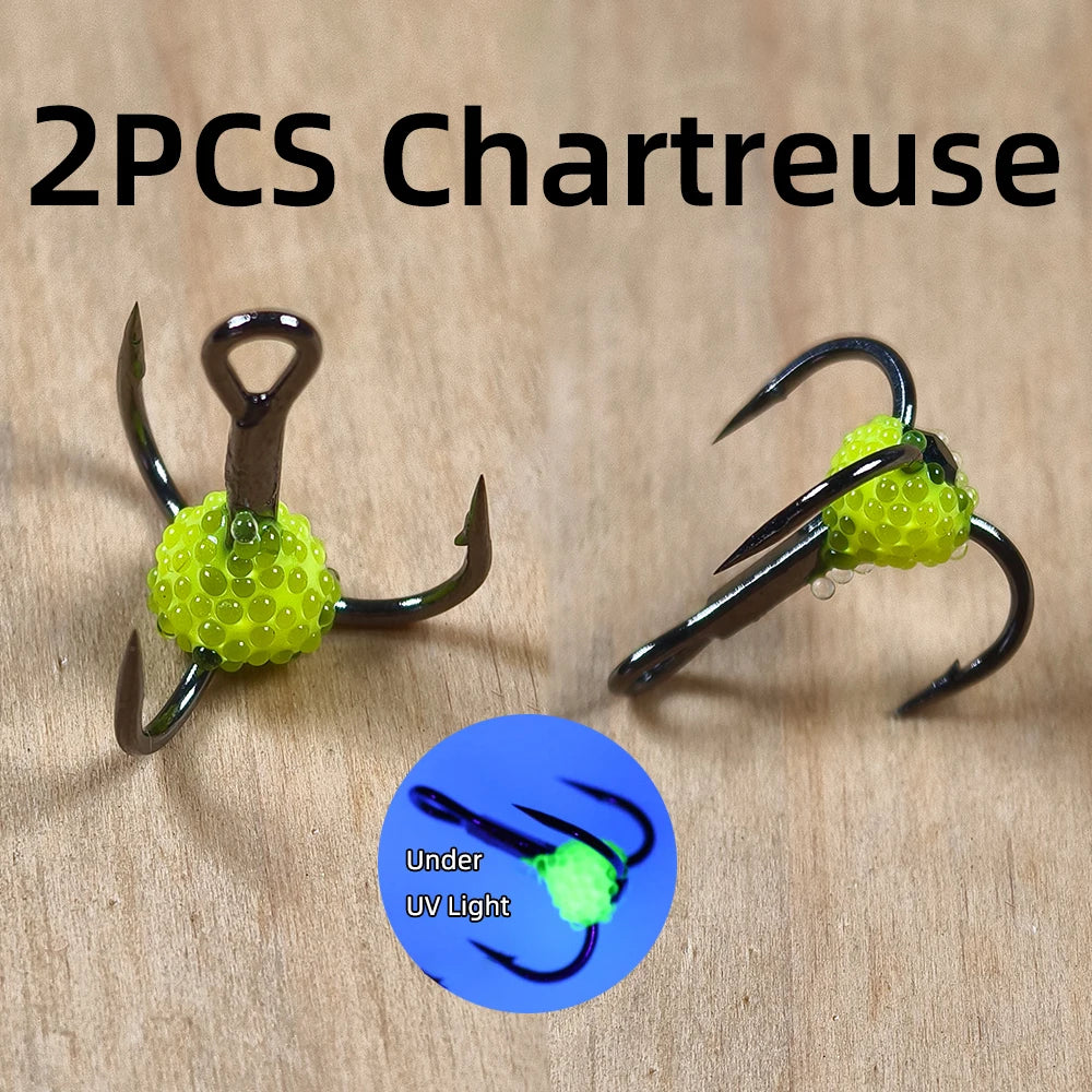Two chartreuse fishing treble hooks with glowing UV beads on wood background, close-up.