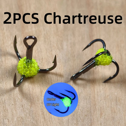 Two chartreuse fishing treble hooks with glowing UV beads on wood background, close-up.