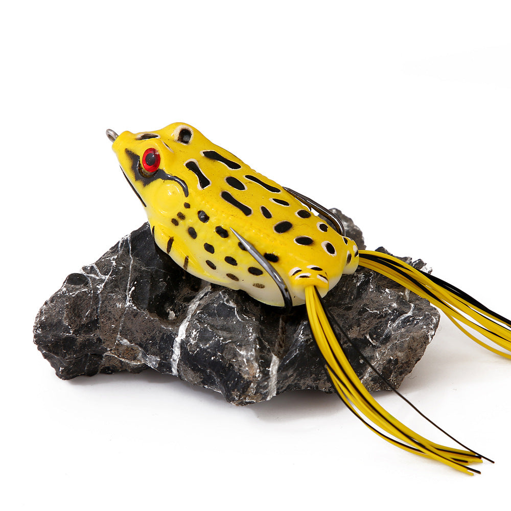 Yellow and black spotted frog fishing lure with skirt tail on a dark rock, outdoor gear
