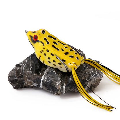 Yellow frog-shaped fishing lure with black spots and long striped legs on a rock