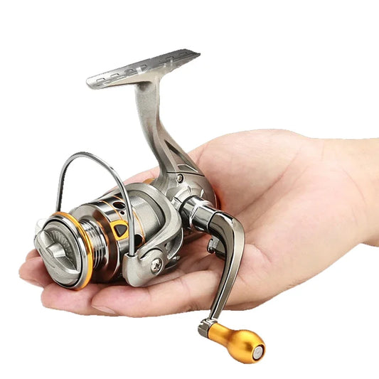 Hand holding compact metallic fishing reel with gold accents, outdoor gear accessory