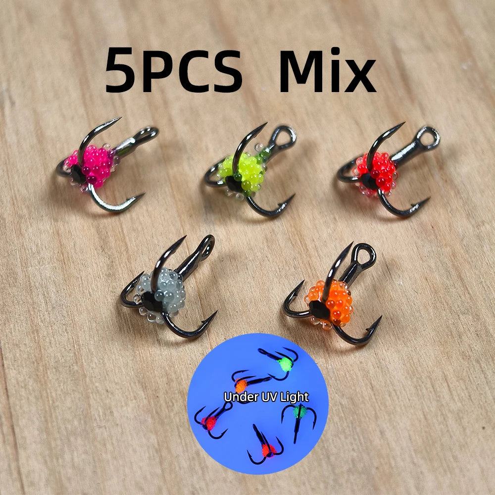 Set of five colorful UV-reactive fishing treble hooks on wooden surface