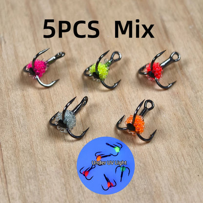 Set of five colorful UV-reactive fishing treble hooks on wooden surface
