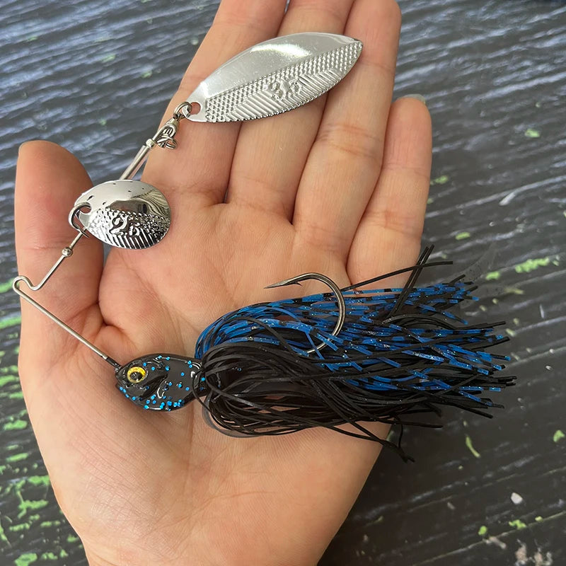Hand holding a blue and black spinnerbait fishing lure with metal blades, outdoor background